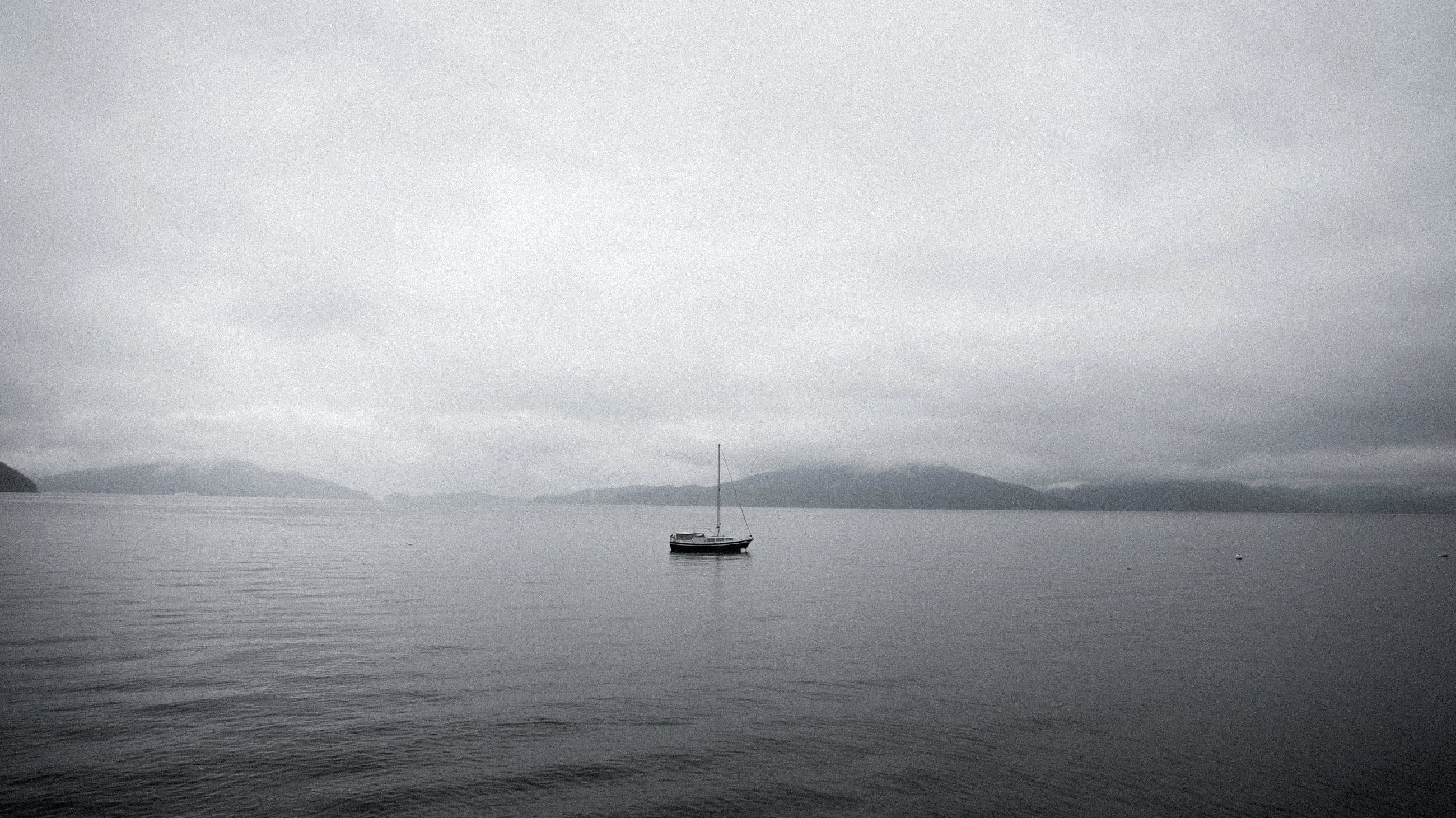 A single sailing yacht at anchor in still water under low cloud